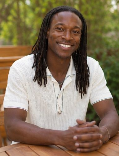 Justin White seated outdoors among greenery, smiling.