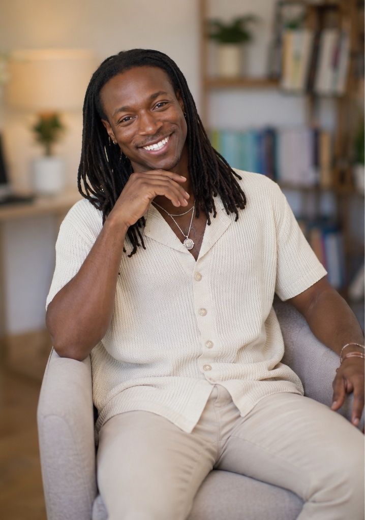 Justin White, seated and smiling, in a warmly lit room lined with books.